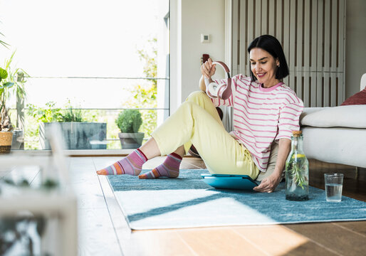 Smiling woman with wireless headphones and tablet PC sitting on rug at home