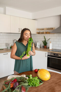 Young woman smelling celery in kitchen