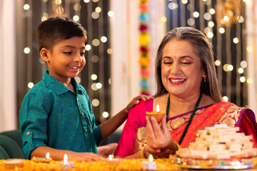 Grandmother and grandson lighting diyas at home during 