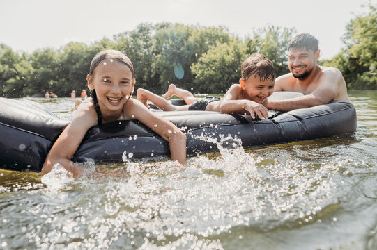 Smiling man with son and daughter floating on pool raft swimming in river