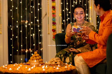 Loving young husband gifting jewelry to beautiful smiling wife while celebrating Diwali festival together at home