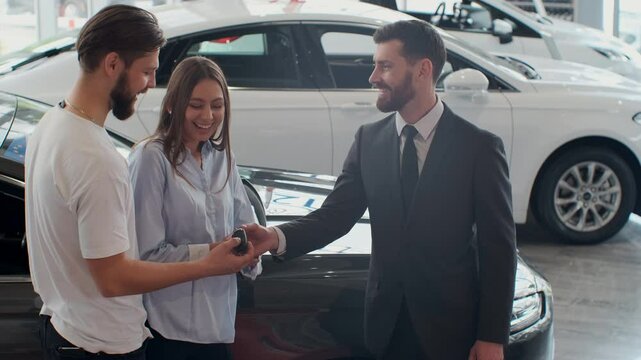 Successful deal between car salesman and young couple in car dealership.