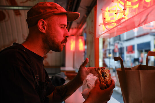 Man eating sandwich near red neon lighting in restaurant