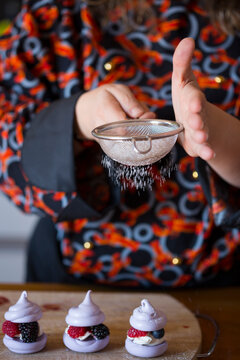 Woman sifting sugar powder on meringue in kitchen