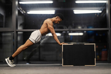 Fototapeta premium Dynamic photo of muscular shirtless black sportsman doing pushups against the box at gym.