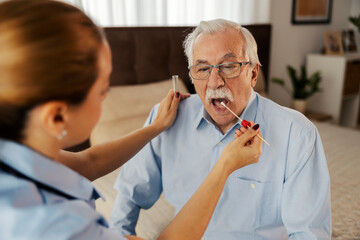 Nurse taking sample with cotton swab from senior man's mouth at her home checkup.