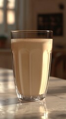 A glass of creamy, light brown beverage on a marble table with soft, natural light shining through the window in the background.