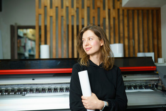 Woman holding rolled up paper and standing near large format machine