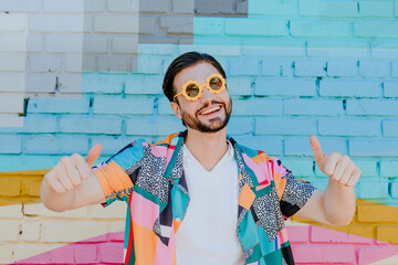 Happy man wearing novelty glasses and gesturing thumbs up in front of brick wall