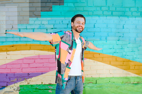 Carefree man with arms outstretched standing in front of multi colored wall