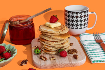 Hand pouring sweet honey onto tasty pancakes on orange background
