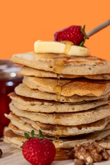 Hand pouring sweet honey onto tasty pancakes on orange background