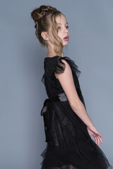 Fototapeta premium A girl gently lifts the sides of her black dress, showing off the dress's sheer layers and ruffled design. The scene emphasizes grace and confidence, showcasing the intersection of fashion and