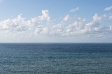 The horizon view of the sea and fluffy white clouds, against a bright blue sky, with little editing.