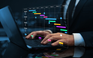 Project manager working on laptop and updating tasks and milestones progress planning with Gantt...
