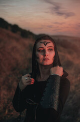 Beautiful girl in black gothic style clothes with tattoo on her face