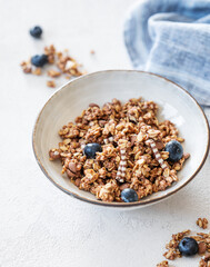 Dry granola with blueberries in a bowl on a light background with fresh berries, napkin and morning sunlight