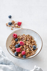 Dry muesli or granola, raspberries and blueberries in a bowl on a light background with fresh berries, napkin and morning sunlight.