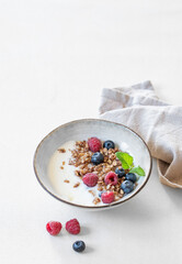 Granola with yogurt, raspberry and blueberries in a bowl on a light background with napkin. Concept of healthy breakfast