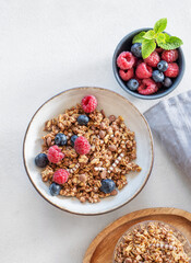 Dry muesli or granola, raspberries and blueberries in a bowl on a light background with fresh berries and morning sunlight.