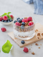 Natural greek yogurt with granola, raspberries and blueberries in a glass on a light background