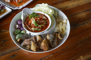 Green Mango Nam prik and Fried gourami served in compartment tray with various kinds of fresh vegetable. High angle view of dining table in Thai restaurant.