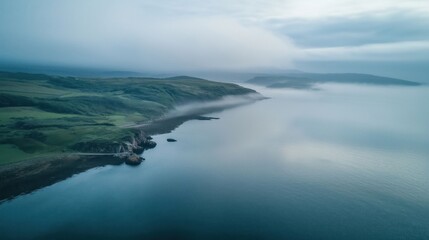 Obraz premium A serene coastal scene with misty hills and calm waters blending into the fog.