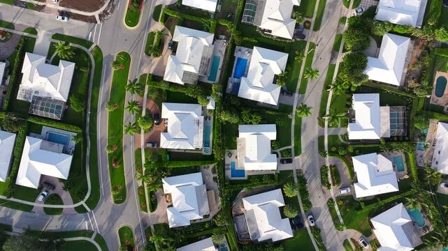 Overhead view of suburban homes with swimming pools and well-maintained yards in Boca Raton, Florida. Curving roads weave through the neighborhood. Aerial.