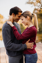 Smiling woman in sweater hugging boyfriend on pier in autumn