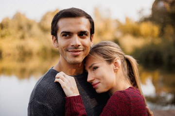 Fototapeta premium Young romantic couple looking away near blurred lake in autumn