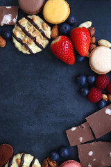 Macarons, chocolate, cookies, berries and various nuts on dark blue background. Top view.