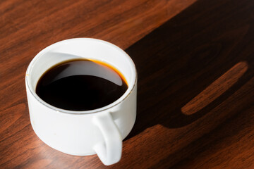 morning black coffee in a white cup and a long shadow from the cup on wooden table