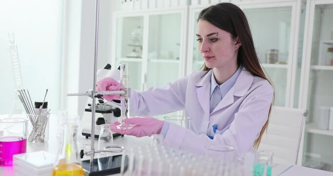 Woman scientist carefully places beaker under burette in laboratory. Female worker in uniform prepares equipment for scientific experiment