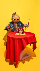 Terrifying person in mask and ripped costume, holding cocktail and fork, while woman head, surrounded by noodles and eyeballs, set on table before him. Halloween, pop art, creativity, party concept