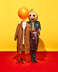 Person in creepy ripped costume and mask, standing next to mannequin dressed in brown coat and shoes against vivid yellow background. Ghost mate. Concept of Halloween, pop art, creativity, party