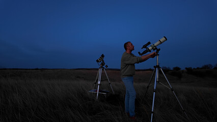 Amateur astronomer looking at the evening skies, observing planets, stars, Moon and other celestial objects with a telescope.