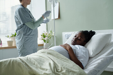 Medical professional providing care to bedridden patient in hospital room with bright window...