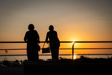 silhouette of two old ladies talking at ocean sunset. socializing senior elderly females share...