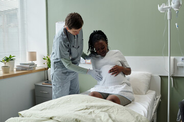 Medical professional assisting pregnant woman in hospital room, providing care and support....