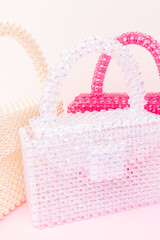Handcraft bags made from shiny beads in front of beige and pink background.