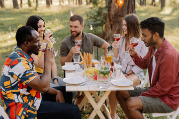 Meeting of multiracial group of friends eating dinner and drinking wine during party in the forest