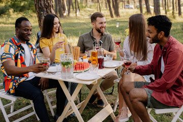 Meeting of multiracial group of friends eating dinner and drinking wine during party in the forest
