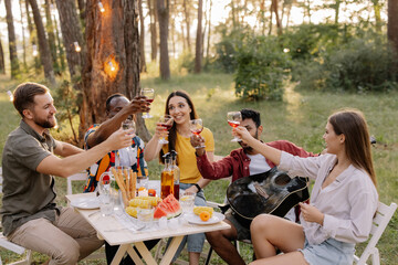 Meeting of multiracial group of friends playing guitar, singing, eating dinner and drinking wine during party in the forest