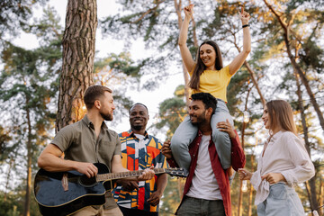 Multiracial group of people, bearded hipster man playing guitar and friends dancing, singing and having fun