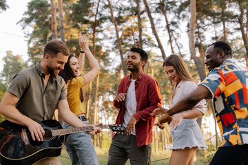 Multiracial group of people, bearded hipster man playing guitar and friends dancing, singing and having fun