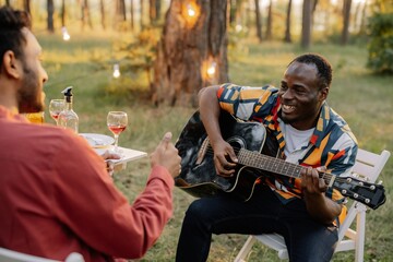 African man plays the guitar for Indian man who drinks wine and sings