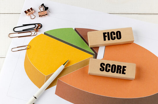 FICO score text on wooden blocks placed on a pie chart with stationery and pen on a white desk