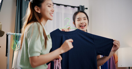 Fototapeta premium Portrait of Two cheerful woman influencers are live streaming to promote a clothing sell during a flash sale on social media or blog in a home studio. Remote shopping, online shopping.