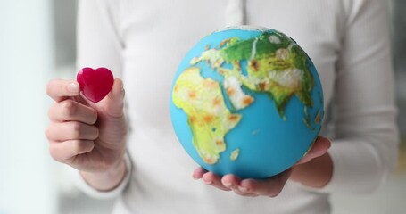 Woman holds small red heart and globe symbolizing love and care for planet. Female ecologist attracts attention to global problems