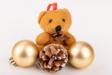 Adorable Christmas bear ornament next to golden balls and pine cone on a white backdrop